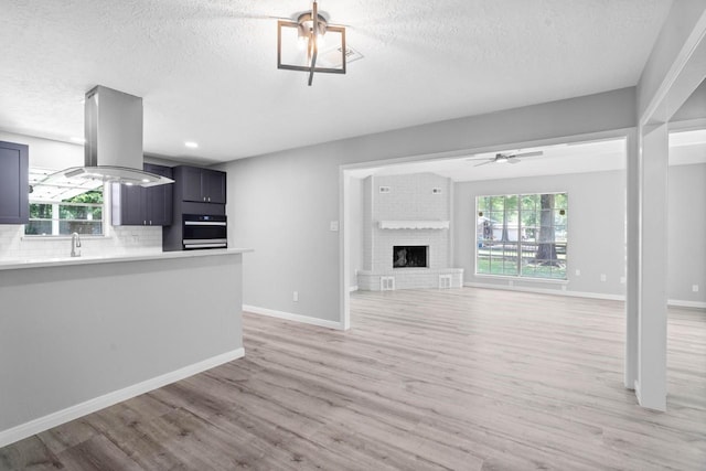 13400 Nicholson Rd, Conroe, TX 77303 - unfurnished living room with a textured ceiling, light wood-style floors, a brick fireplace, and ceiling fan