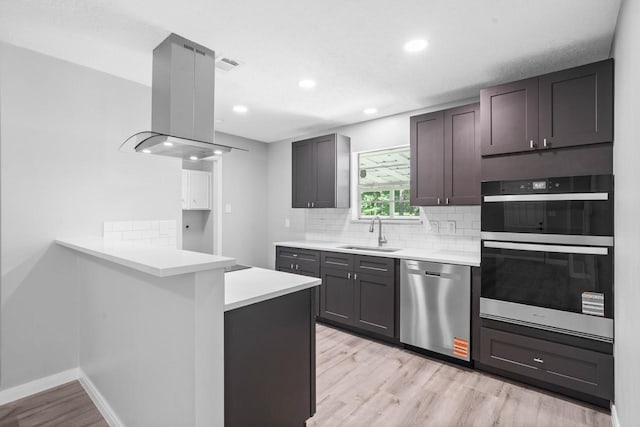 13400 Nicholson Rd, Conroe, TX 77303 - kitchen featuring stainless steel appliances, island range hood, light wood finished floors, tasteful backsplash, and light countertops