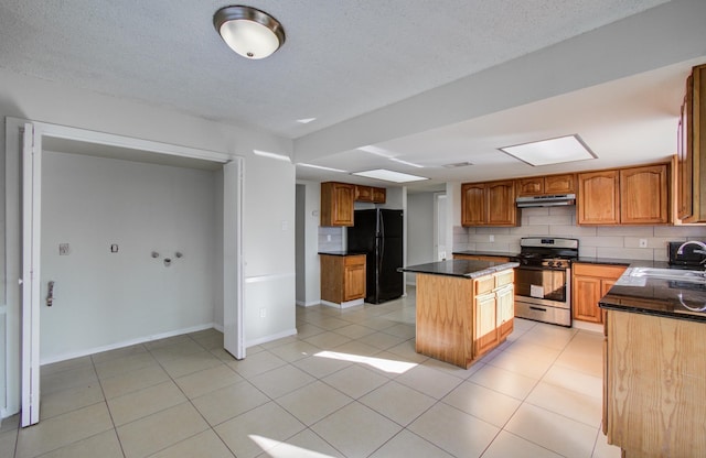 11307 Birdwing Ln, Houston, TX 77067 - kitchen with under cabinet range hood, stainless steel gas stove, freestanding refrigerator, and backsplash
