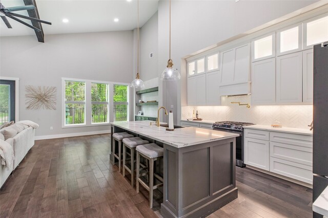 kitchen featuring a sink, stainless steel range with gas cooktop, baseboards, decorative backsplash, and high vaulted ceiling
