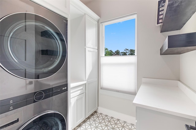 laundry room featuring cabinet space, stacked washing maching and dryer, and baseboards