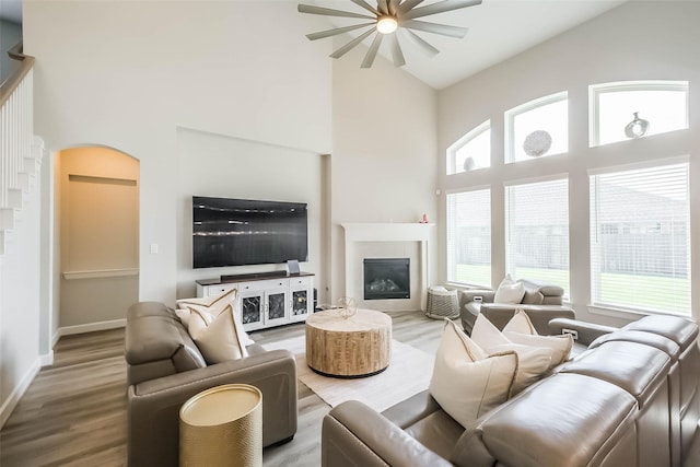 living area featuring wood finished floors, arched walkways, ceiling fan, a glass covered fireplace, and a high ceiling