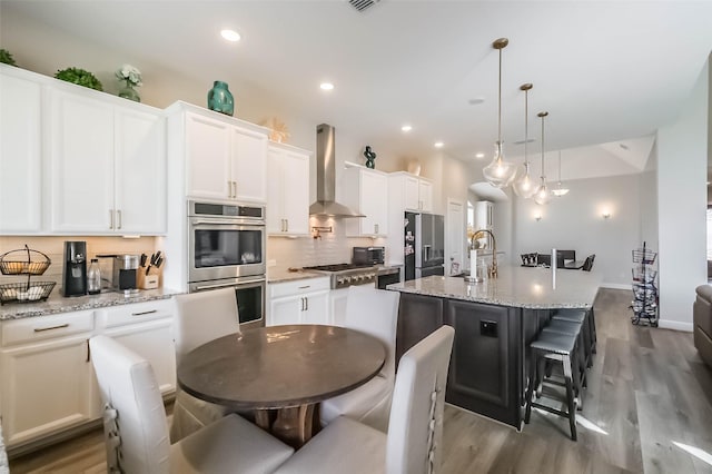 kitchen with tasteful backsplash, stainless steel appliances, wall chimney range hood, light wood finished floors, and a sink