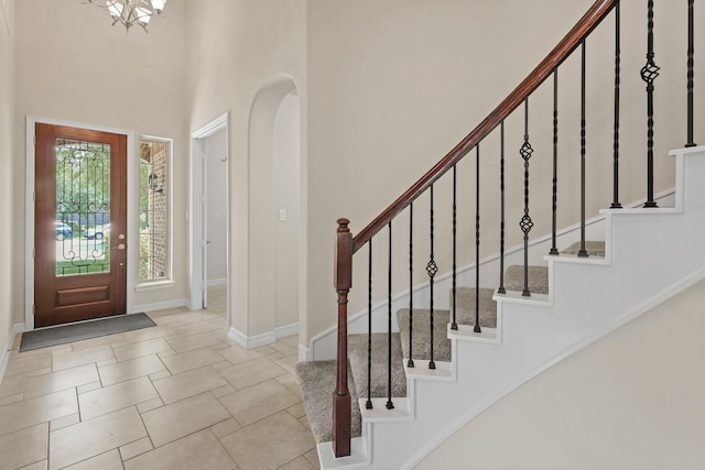 entryway with stairs, arched walkways, a towering ceiling, baseboards, and a notable chandelier