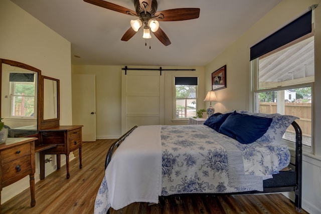 bedroom with a barn door, a ceiling fan, wood finished floors, and multiple windows