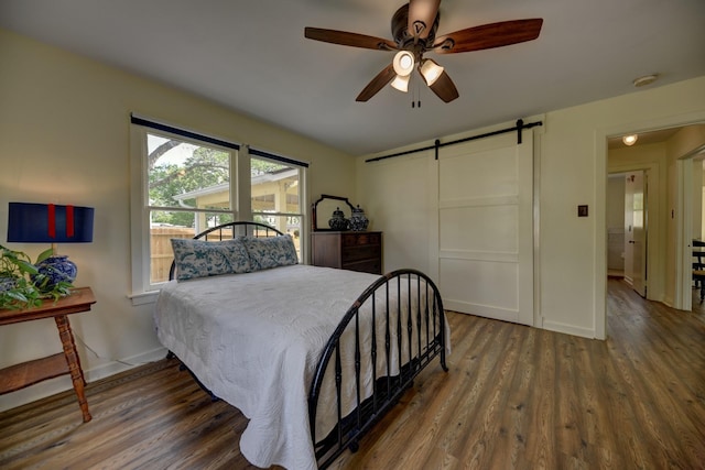 bedroom with baseboards, a ceiling fan, wood finished floors, and a barn door