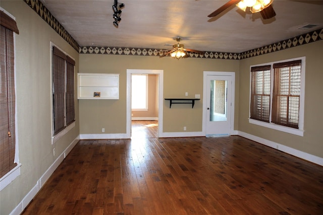 unfurnished room with baseboards, a ceiling fan, visible vents, and dark wood finished floors