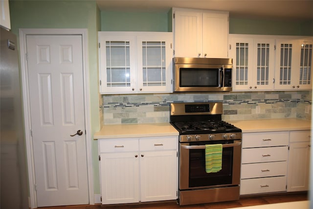 kitchen featuring white cabinets, stainless steel appliances, backsplash, glass insert cabinets, and light countertops