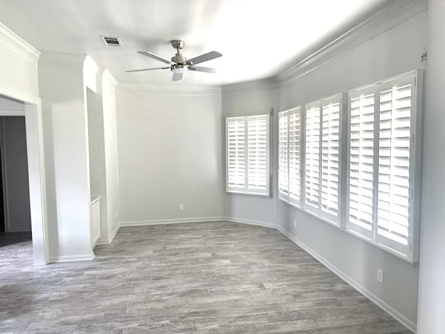 empty room featuring ceiling fan, visible vents, wood finished floors, baseboards, and ornamental molding