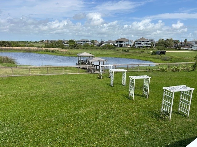 view of dock featuring a lawn, a water view, and fence