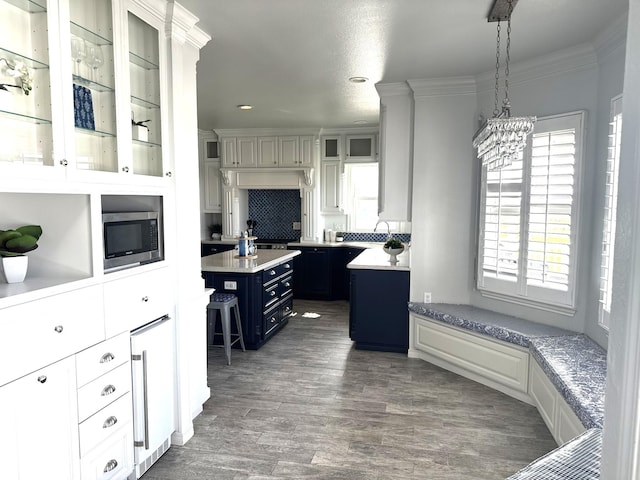 12924 Stewart Rd, Galveston, TX 77554 - kitchen with stainless steel microwave, blue cabinets, light countertops, dark wood-style floors, and glass insert cabinets