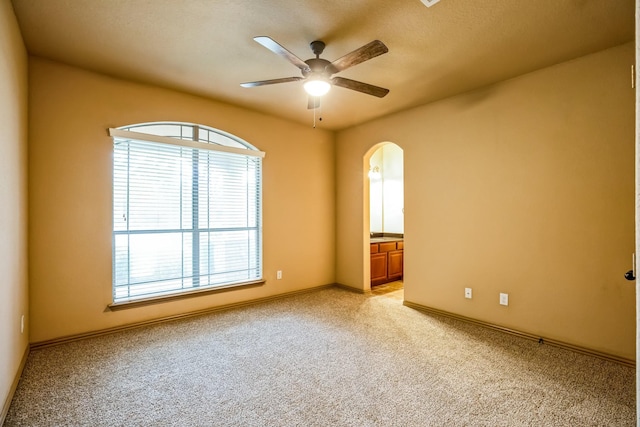 unfurnished room featuring ceiling fan, arched walkways, baseboards, and light carpet