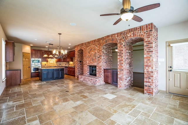 kitchen with stainless steel appliances, stone tile floors, open floor plan, ceiling fan with notable chandelier, and a kitchen island