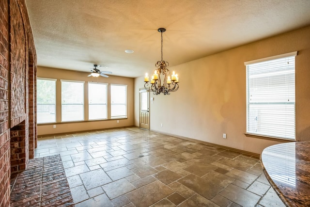 interior space featuring ceiling fan with notable chandelier, baseboards, stone tile flooring, and a textured ceiling