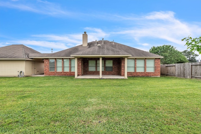 back of property featuring a chimney, fence, brick siding, a lawn, and a patio