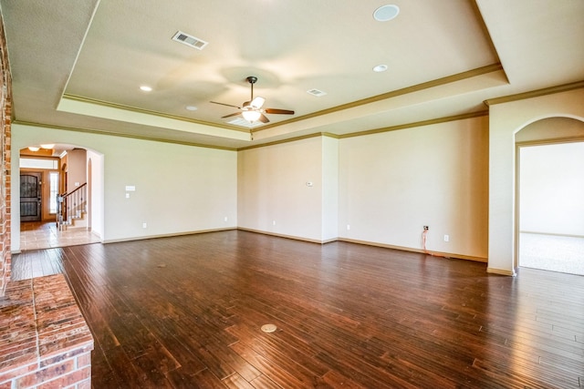 unfurnished living room with a tray ceiling, arched walkways, visible vents, and crown molding