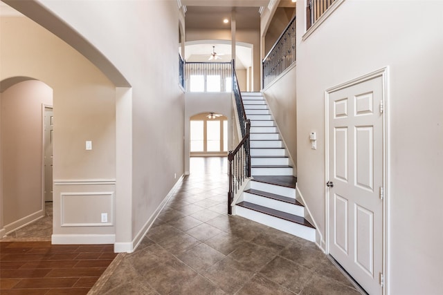 interior space with arched walkways, ceiling fan, baseboards, and a high ceiling