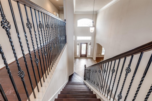 staircase featuring ornamental molding, wood finished floors, baseboards, a high ceiling, and arched walkways