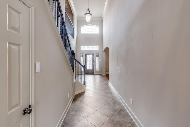 foyer featuring arched walkways, light tile patterned floors, baseboards, ornamental molding, and stairs