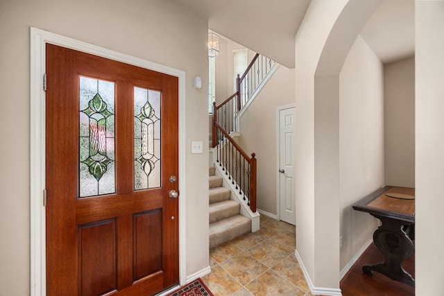 entrance foyer featuring baseboards, arched walkways, and stairs
