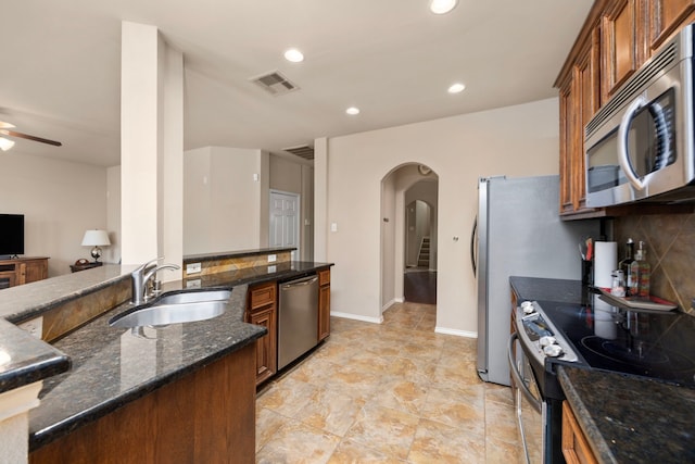 kitchen with arched walkways, brown cabinetry, appliances with stainless steel finishes, and a sink