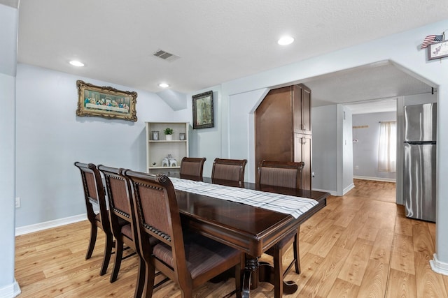 dining area featuring arched walkways, visible vents, light wood finished floors, and baseboards