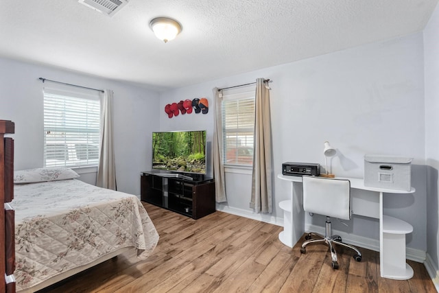 bedroom with baseboards, wood finished floors, visible vents, and a textured ceiling