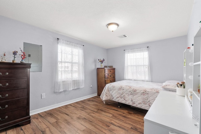bedroom with electric panel, wood finished floors, visible vents, and multiple windows