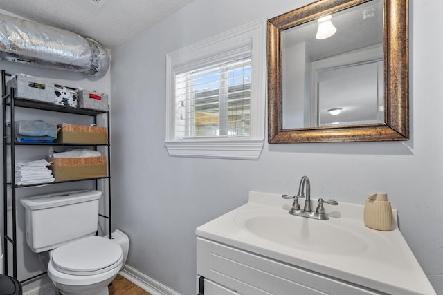 half bath featuring a textured ceiling, toilet, baseboards, wood finished floors, and vanity