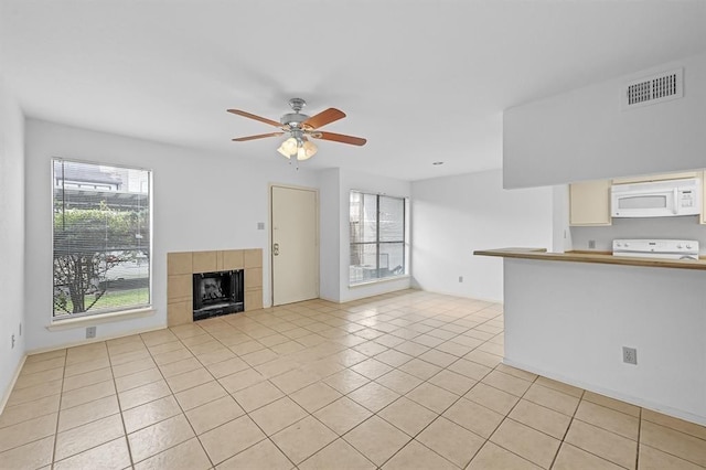 unfurnished living room featuring plenty of natural light, a ceiling fan, visible vents, and light tile patterned floors