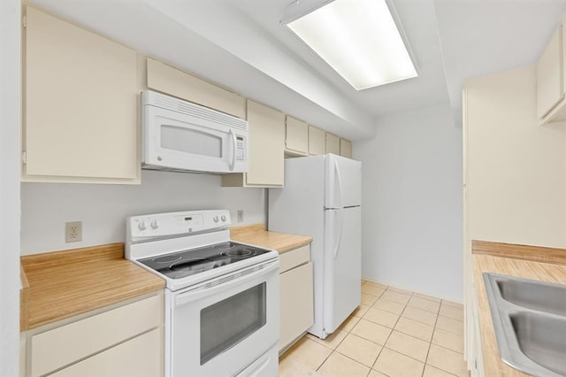 kitchen with a sink, light tile patterned flooring, white appliances, cream cabinets, and light countertops