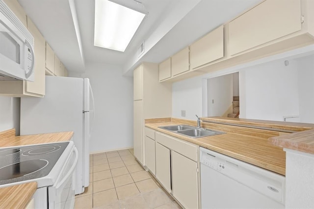 kitchen featuring light countertops, a sink, light tile patterned flooring, white appliances, and cream cabinets