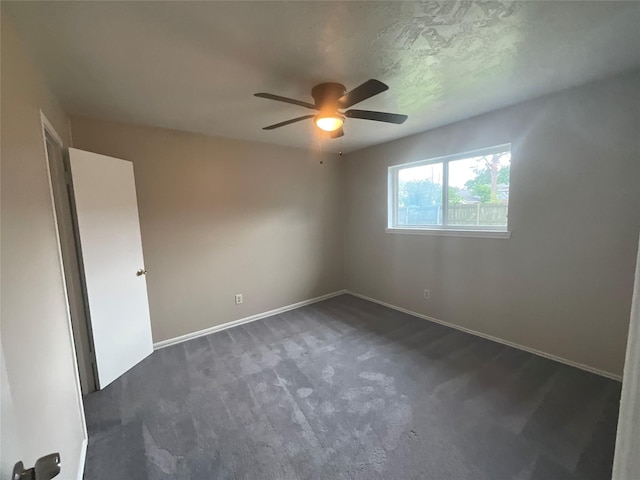 empty room with dark carpet, baseboards, and ceiling fan