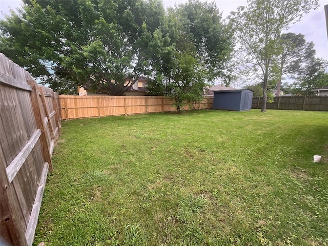 view of yard with a fenced backyard, a storage unit, and an outbuilding