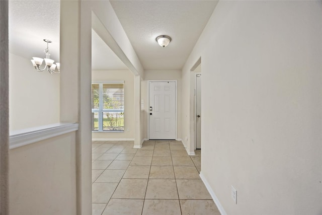 entryway with baseboards, a textured ceiling, a chandelier, and light tile patterned floors