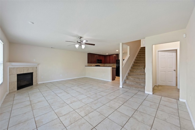 unfurnished living room featuring light tile patterned flooring, baseboards, a tiled fireplace, stairs, and ceiling fan