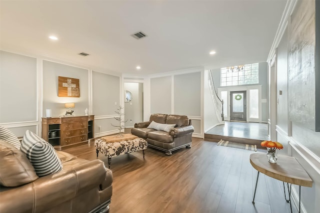 living room featuring recessed lighting, a decorative wall, wood finished floors, and visible vents