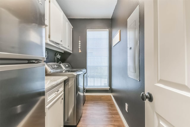 laundry area with wood finished floors, electric panel, cabinet space, baseboards, and independent washer and dryer