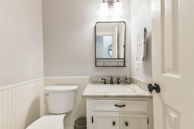 half bath with wainscoting, vanity, and toilet