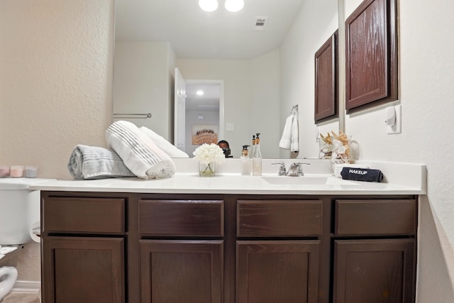 bathroom with a textured wall, visible vents, toilet, and vanity