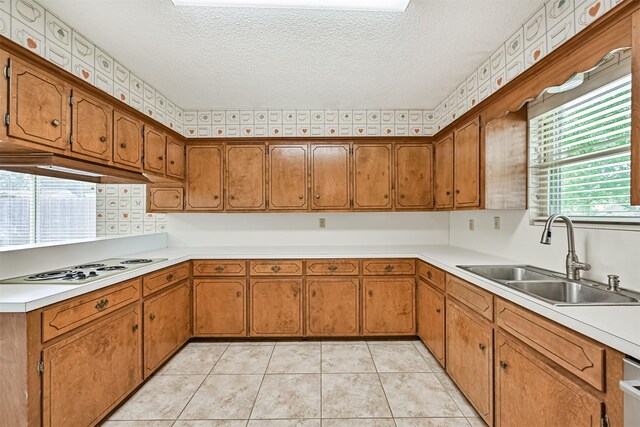 kitchen featuring a textured ceiling, brown cabinetry, a sink, and white electric cooktop