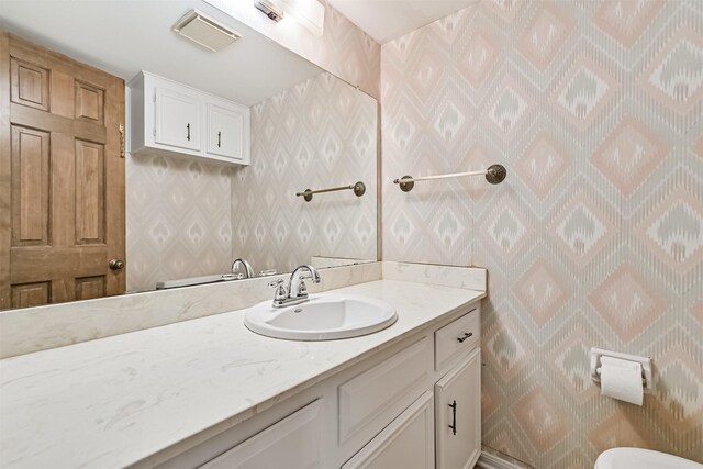 half bath with vanity, toilet, wallpapered walls, and visible vents