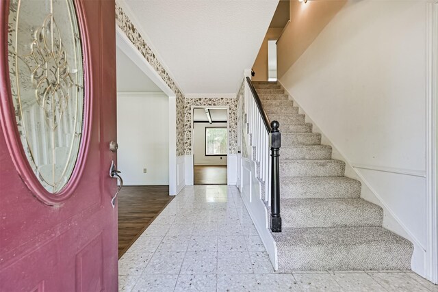 entryway featuring crown molding, a wainscoted wall, a decorative wall, and stairs