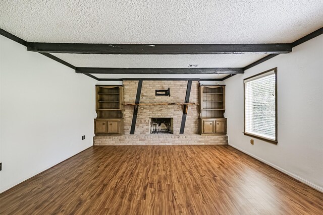 unfurnished living room with a textured ceiling, beam ceiling, and wood finished floors