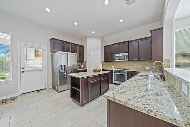 kitchen with light stone counters, dark brown cabinets, a sink, decorative backsplash, and stainless steel appliances