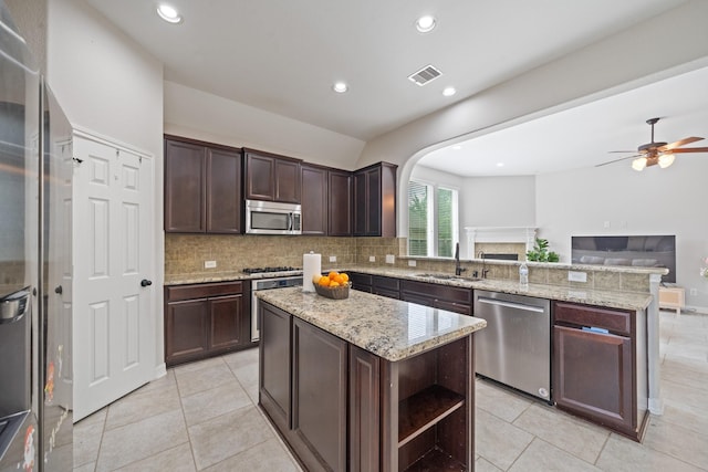kitchen featuring stainless steel appliances, a sink, a peninsula, tasteful backsplash, and open floor plan