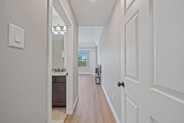 hallway featuring light wood-type flooring, a textured wall, and baseboards