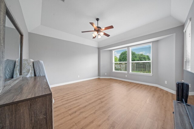 unfurnished living room featuring baseboards, a ceiling fan, a tray ceiling, and light wood-type flooring