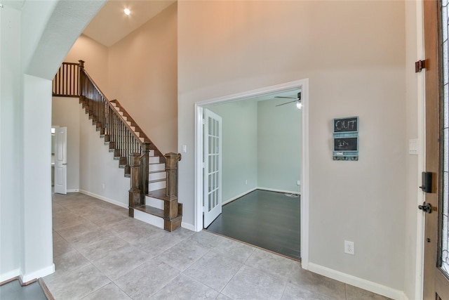 tiled entrance foyer with stairway, a towering ceiling, baseboards, and a ceiling fan