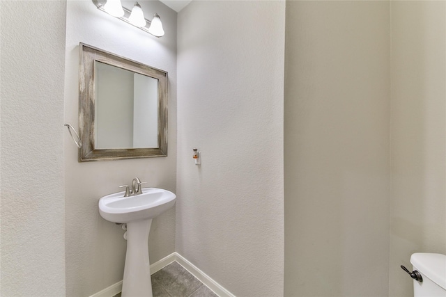 half bathroom featuring tile patterned flooring, baseboards, toilet, and a sink